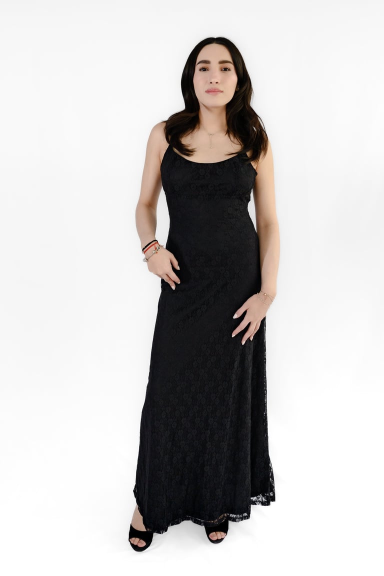 Woman wearing a black lace sleeveless maxi dress with black sandals, standing against a white background