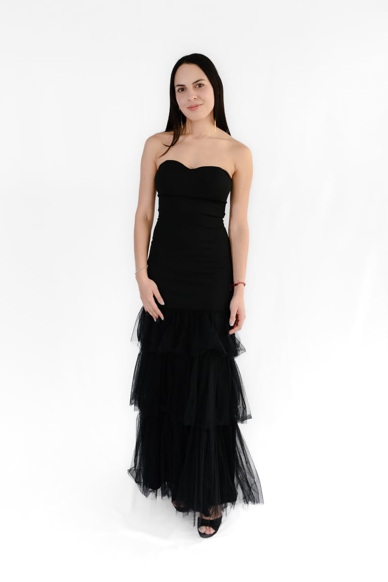 Woman wearing a black strapless sweetheart neckline gown with layered tulle skirt and black heels