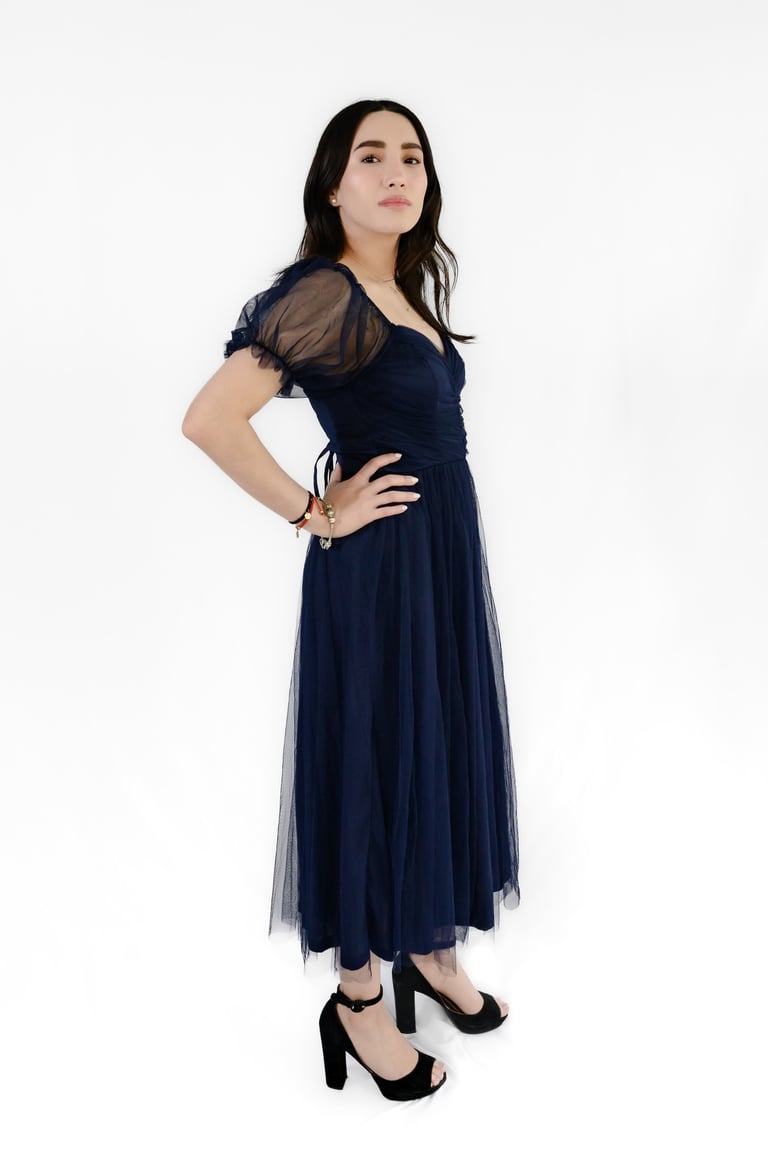 Woman wearing a navy blue wrap dress with sheer sleeves and black platform heels, posed against a white background