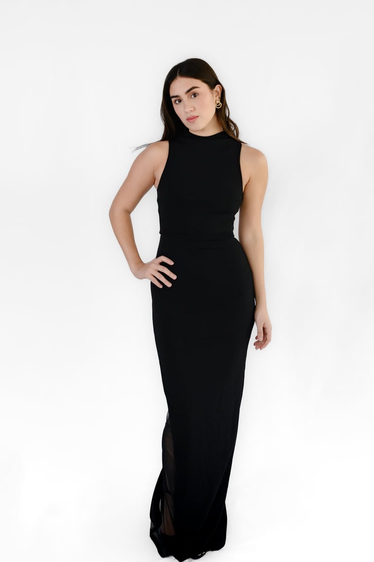Woman in a sleeveless black floor-length gown standing against a white background
