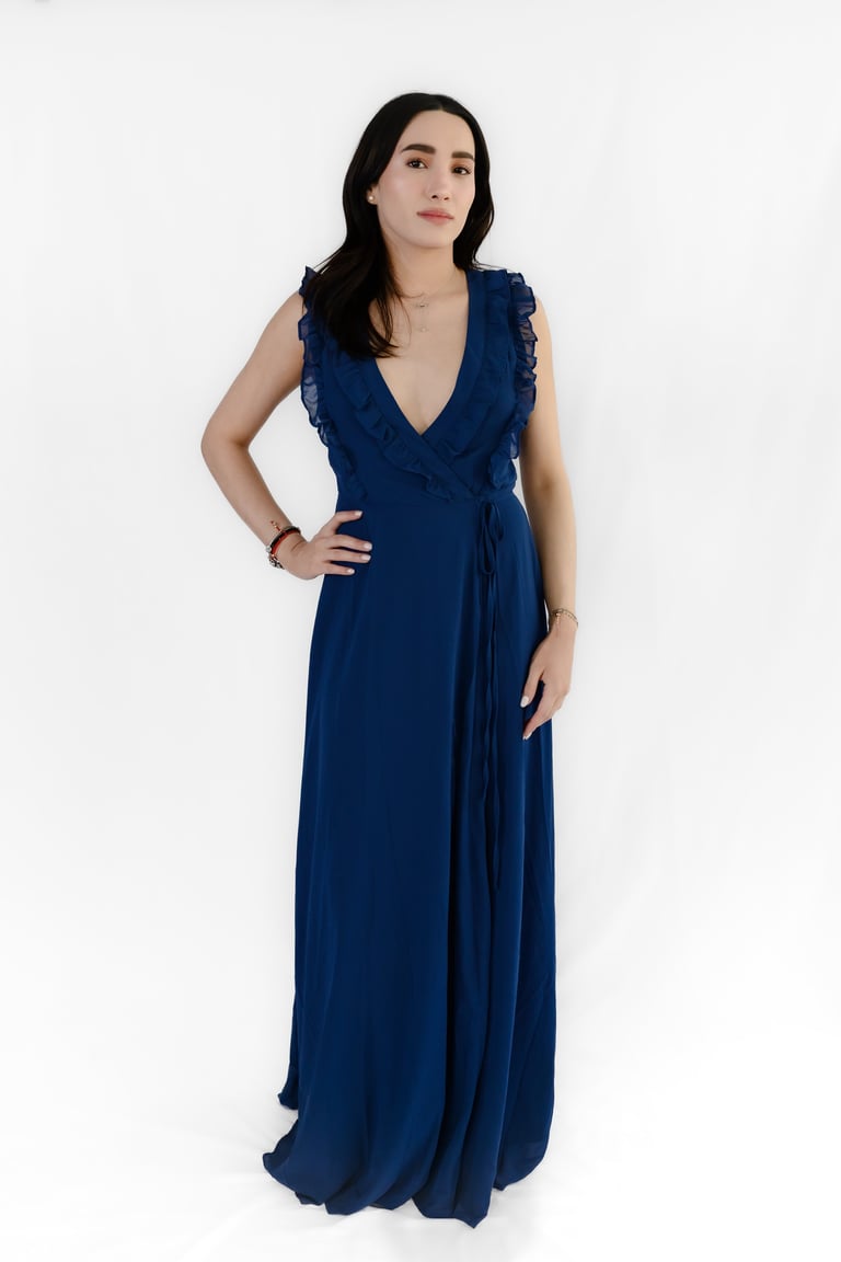 Woman wearing an elegant navy blue sleeveless wrap dress with ruffled neckline against a white background