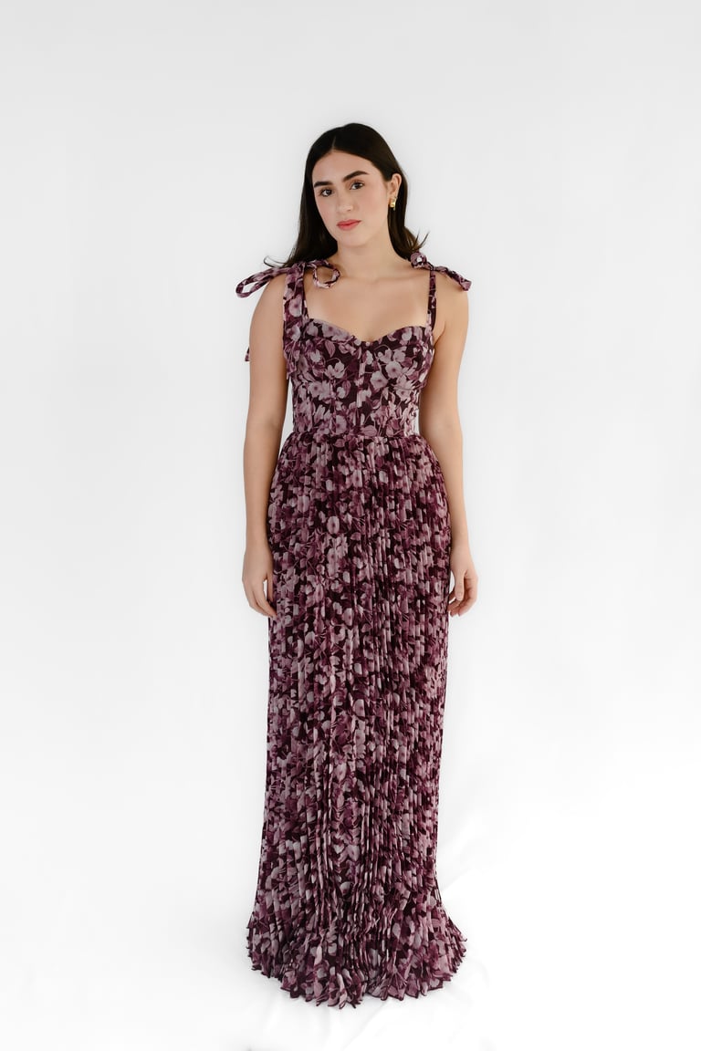 Woman wearing a burgundy floral pleated maxi dress with tie-shoulder straps against a white background