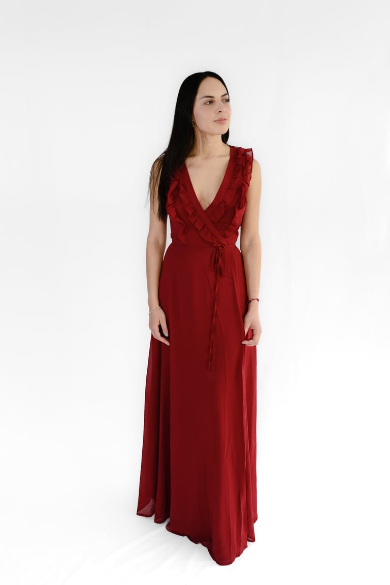 Woman wearing a deep red wrap-style maxi dress standing against a white background