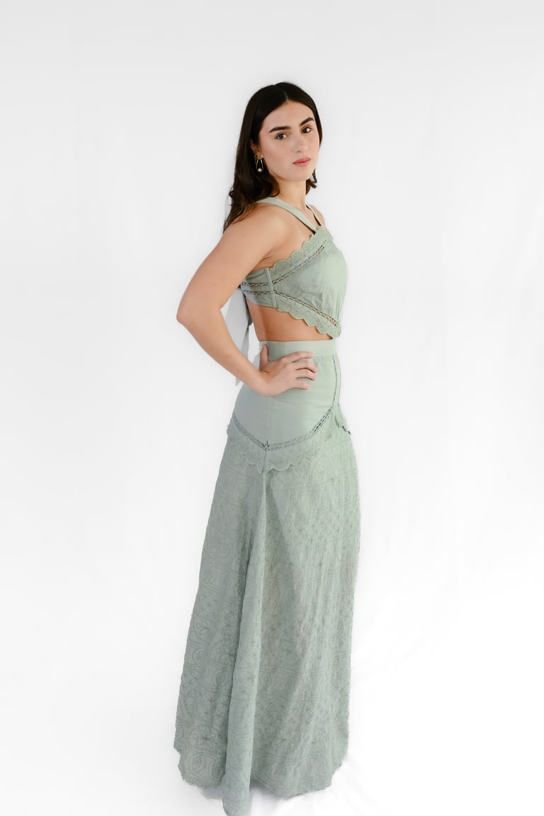 Woman wearing a sage green two-piece dress with crop top and long skirt, posing against white background
