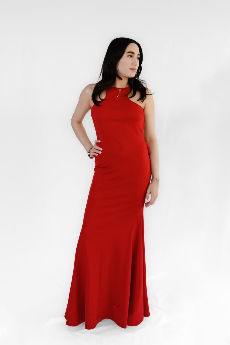 Woman with long black hair wearing a sleeveless red floor-length dress against a white background